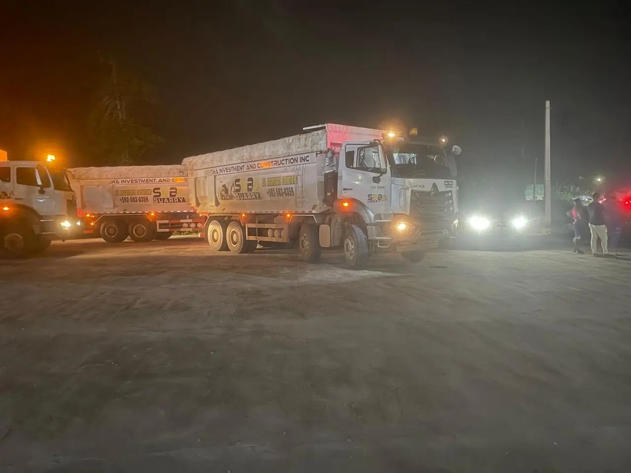 A SEBA-branded HOWO tipper at night, headlights cutting through dust on the quarry haul road.
